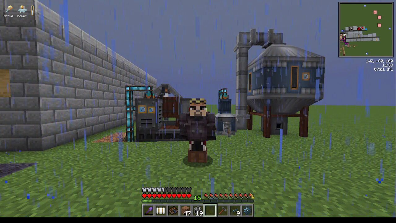 Minecraft scene: player in dark armor standing in rain beside industrial machines and a stone wall on a grassy plain, mini-map in corner.