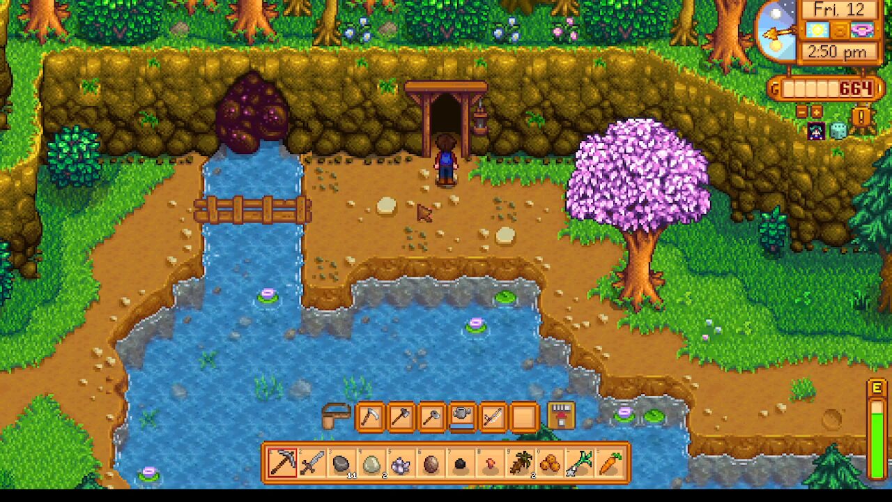 Pixel art game scene: a character stands at a cave entrance beside a small waterfall and a pink-leaved tree, in a colorful forest setting.