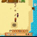 Top-down beach scene: two characters stand on sand near a small circular stone pit, with a wooden shack up ahead and a blue river on the right.