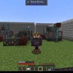 Minecraft scene showing a player standing on grass in a fenced area with industrial machines and pipes against stone brick walls in the background.